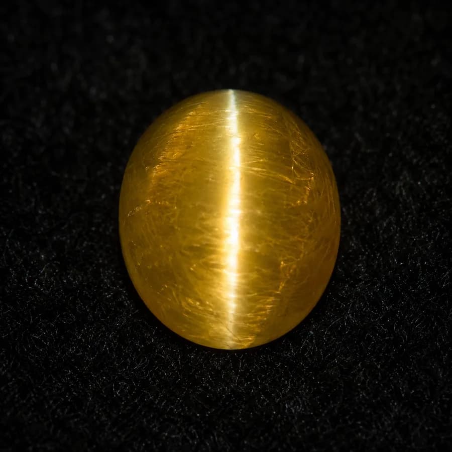 Honey-coloured cat’s eye chrysoberyl cabochon with a single sharp band of light, face-up on black cloth