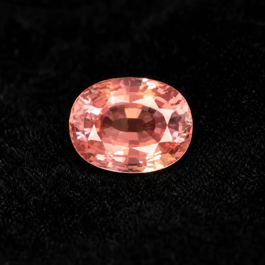 Oval padparadscha sapphire in delicate pinkish orange, face-up on black lace
